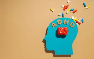 Blue profile silhouette of a head with a red brain and the letters ADHD above it, pills spilling outward to illustrate ADHD treatment awareness.